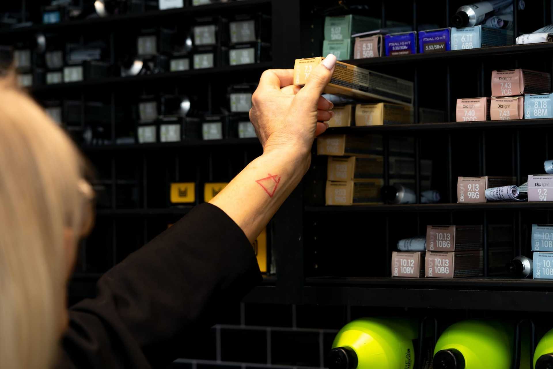 Person selecting hair color from a shelf stocked with various shades and bottles.