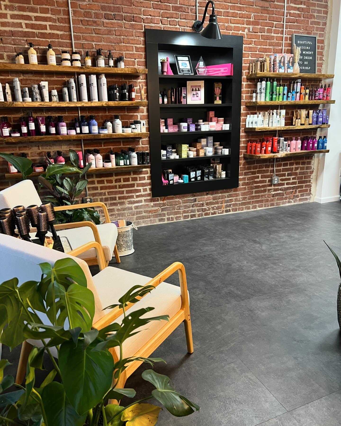 Salon waiting area with shelves of hair products against a brick wall.